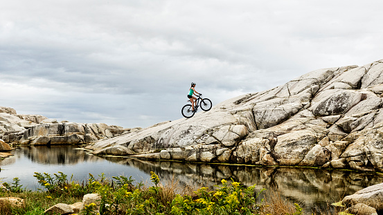 Woman on mountain bike riding up rock face hill in Nova Scotia