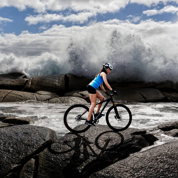 Woman on mountain bike with ocean waves splashing in the background in Nova Scotia.