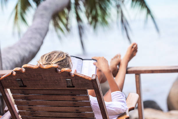 istock Young woman reading a book while relaxing on tropical island 675677476