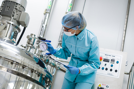 bended scientist in blue lab uniform check how compressor tank works, tablet in hands, close