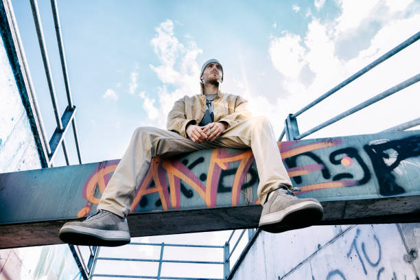 a rap singer on a concrete beam in a subway with graffiti in the background