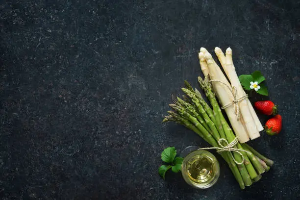 Fresh green and white asparagus with strawberries and wineglas on dark background