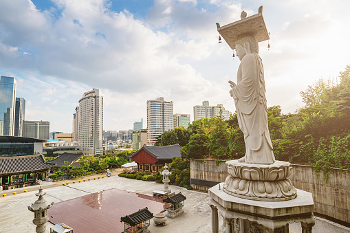 Famous Bongeunsa Temple Buddha Statue. Modern Skyscrspers of downtown Seoul in the background under blue summer sky. Half aerial view from the jungle behind the temple.  Bongeunsa is a buddhist temple located in Seoul, South Korea, Asia.