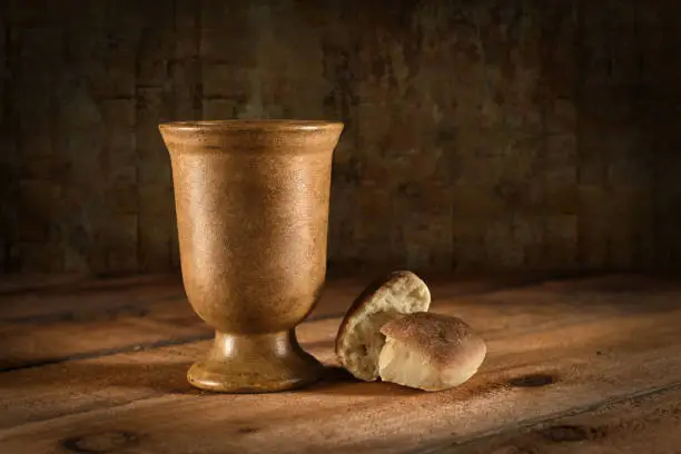 Wine goblet and bread as symbols of Communion on wooden table