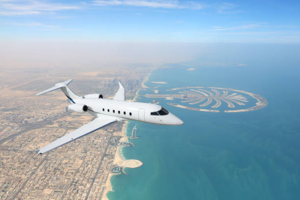 Business jet airplane flying over Dubai city and sea coastline. stock photo