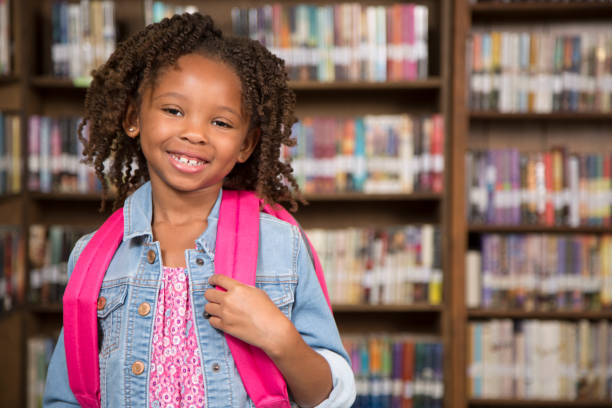 istock African descent little girl in school library with backpack. 675774120