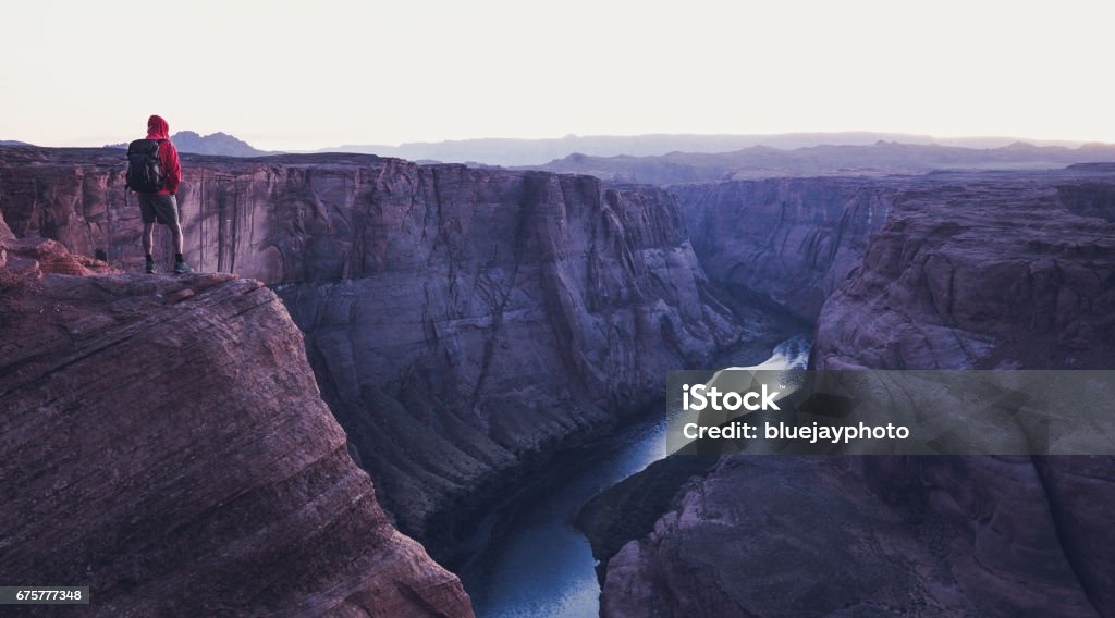 Male hiker overlooking Horseshoe Bend in twilight, Arizona, USA A male hiker is standing on steep cliffs enjoying the beautiful view of Colorado river flowing at famous Horseshoe Bend overlook in mystic post sunset twilight during blue hour in summer, Arizona, USA Canyon Stock Photo