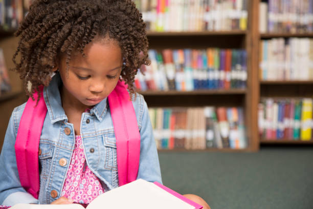 istock African descent little girl in school library reading book. 675779846