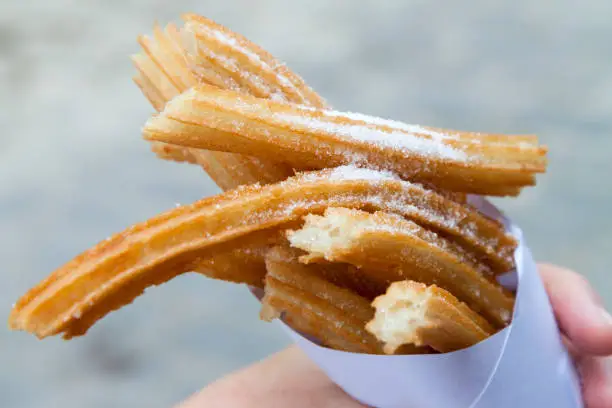 Churros sprinkled with sugar held in a paper cone