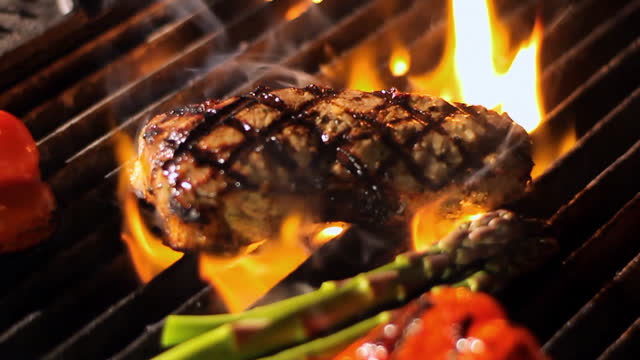 A steak gets placed on a fiery grill.