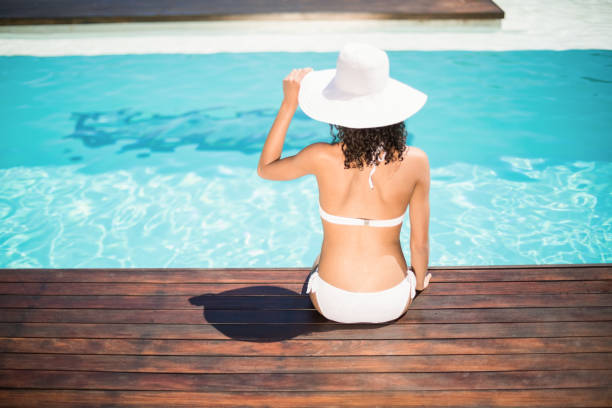 rear view of woman wearing white bikini and hat sitting near pool - teenage girls rear view women sensuality imagens e fotografias de stock