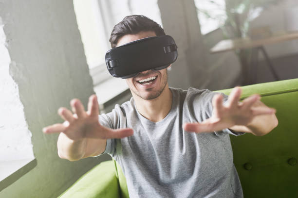 istock Close up portrait of astonished handsome guy experiencing virtual reality while using VR set headset for entertaining, sitting on couch at home. People, technology and innovation concept 675823794