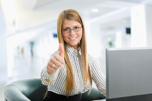 Young smiling woman working in office. About 20 years old, Caucasian blonde with glasses working on computer.