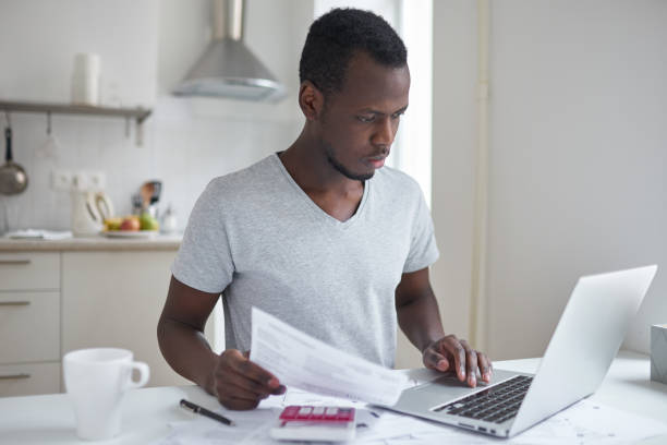 istock Concentrated young african american student using online banking application with hand on touchpad, looking at screen of his laptop, trying to make payment for university education. Financial problems 675895860