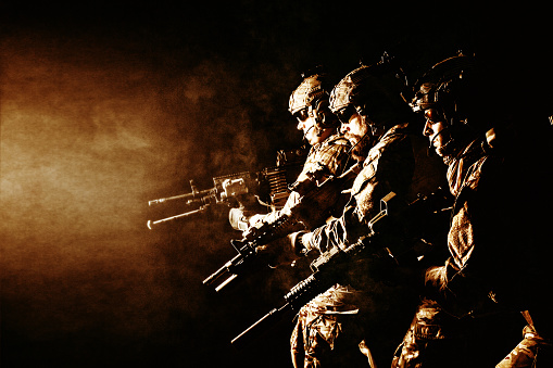 Group of security forces in Combat Uniforms with rifles, lined in the face of danger. Facing enemy, they stand boldly and ready to protect the nation. Studio contour silhouette shot, backlight, profile side view