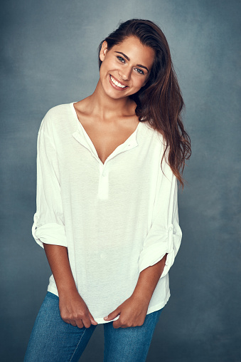 Portrait of a beautiful young woman smiling against a gray background in studio