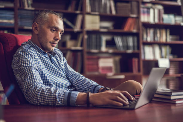 empresario adulto medio trabajando en ordenador portátil en casa biblioteca. - professor librarian university library fotografías e imágenes de stock