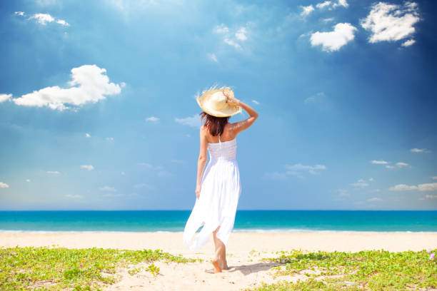 beautiful young woman standing on the sand beach and looking at the sea stock photo