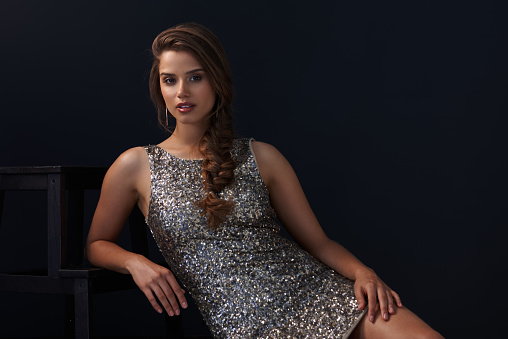 Portrait of a beautiful young woman in a sequined dress posing against a dark background