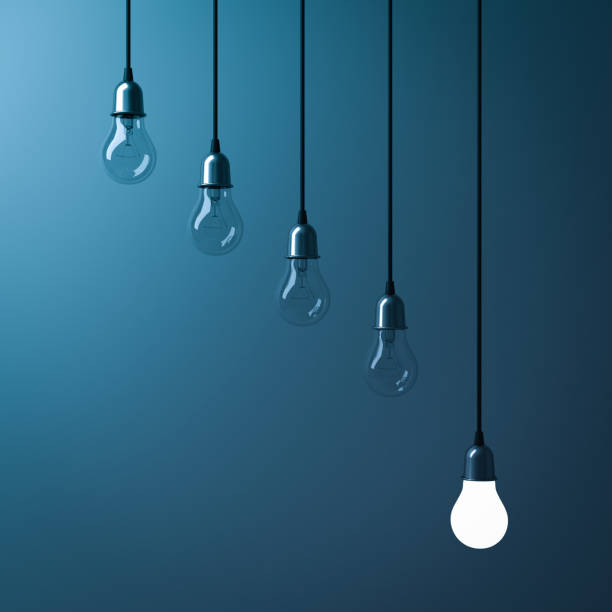 istock One hanging light bulb glowing different and standing out from unlit incandescent bulbs with reflection on dark cyan background , leadership and different business creative idea concept. 3D render 675955724