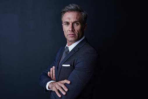 Studio portrait of a confident and mature businessman standing against a dark background