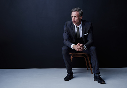 Studio shot of a mature businessman sitting on a chair against a dark background