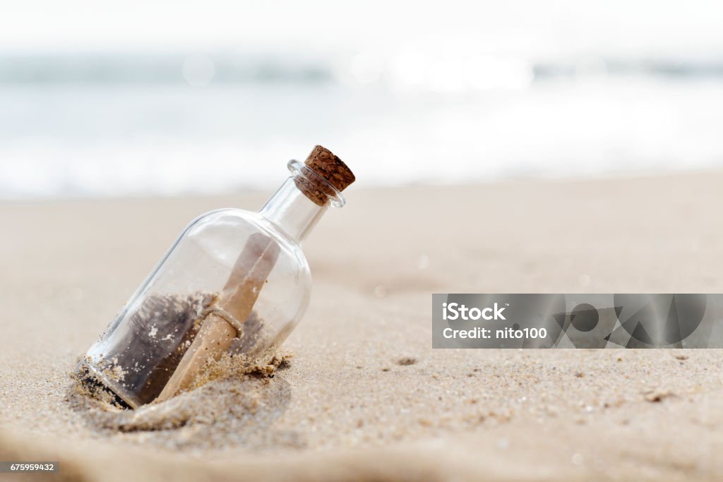 message in a bottle closeup of a glass bottle with a rolled message inside stranded in the sand of a lonely beach Message in a Bottle Stock Photo