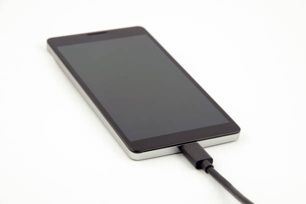 istock Closeup view of a mobile phone - smartphone - with attached black charging cable on a white background 675968988