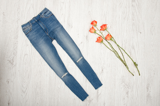 Blue jeans and orange roses on a wooden background. Fashionable concept, top view