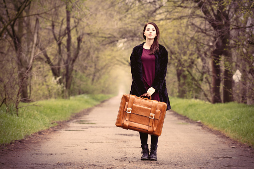 beautiful young woman with brown suitcase standing in the middle on the road
