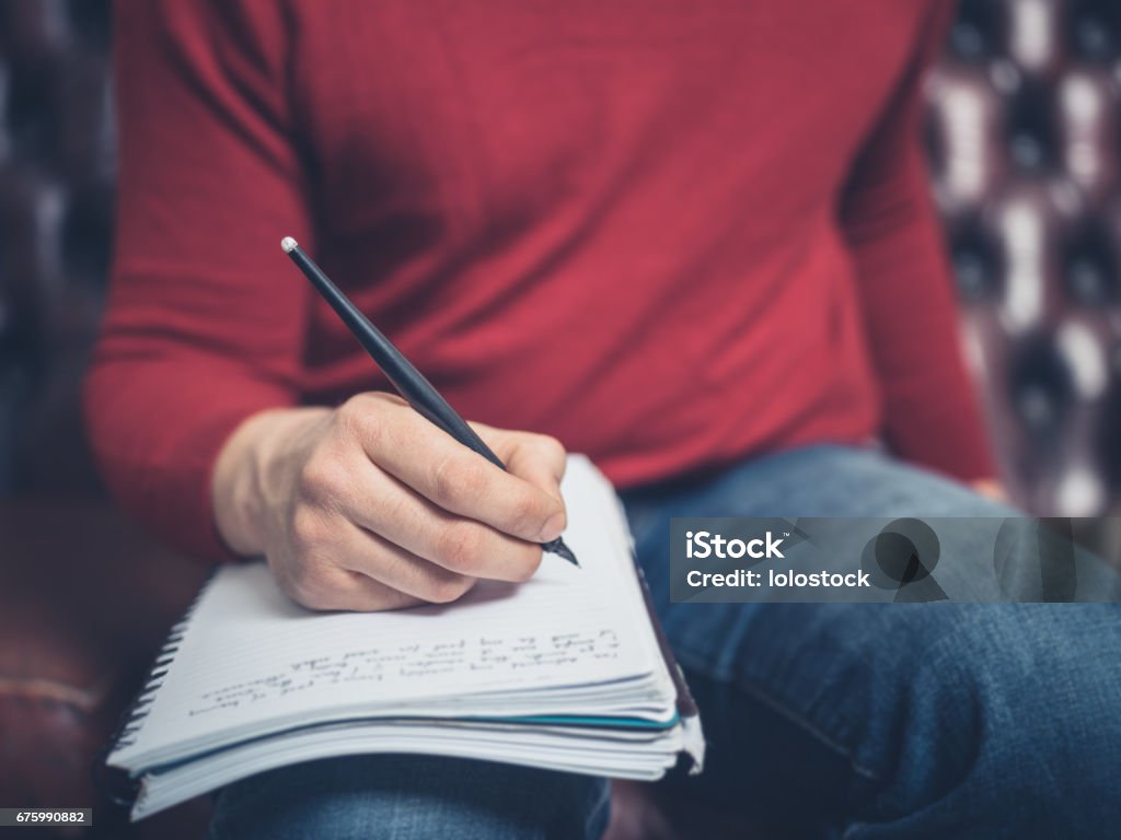 Man on sofa writing in notebook Close up on a man sitting on a sofa and writing in a notebook Men Stock Photo