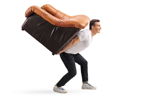 Young guy carrying an armchair on his back Profile shot of a young guy carrying an armchair on his back isolated on white background carrying stock pictures, royalty-free photos & images