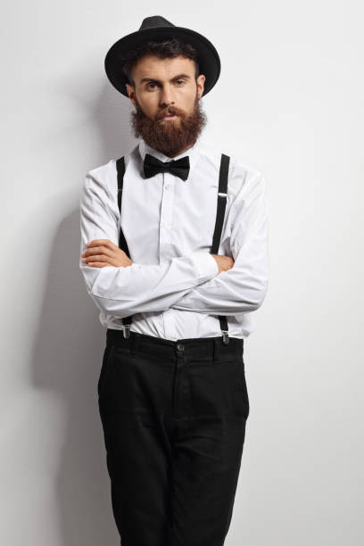 istock Bearded man with a bow tie and suspenders leaning against a wall 675994352