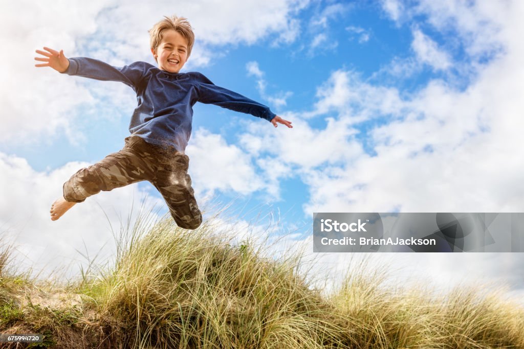 Boy leaping and jumping over sand dunes on beach vacation Boy jumping over sand dunes on beach vacation Child Stock Photo