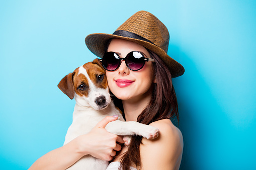 beautiful young woman with her dog standing in front of wonderful blue background