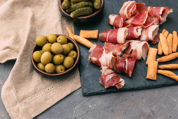 istock Typical spanish tapas concept. Concept include variety slices jamon, chorizo, salami, bowls with olives, peppers, anchovies, spicy potatoes 676008568