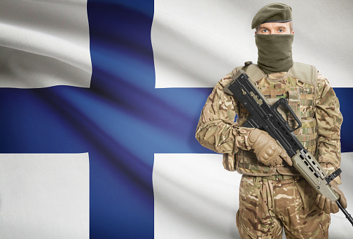 Soldier holding machine gun with national flag on background - Finland
