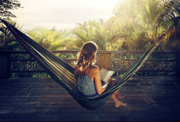 mulher em um livro de leitura de vestido numa rede na selva ao pôr do sol. - summer women hammock nature - fotografias e filmes do acervo