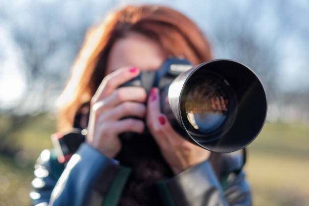 The girl holds a camera in her hands and takes a picture with enthusiasm. She walks in nature on a bright sunny day.