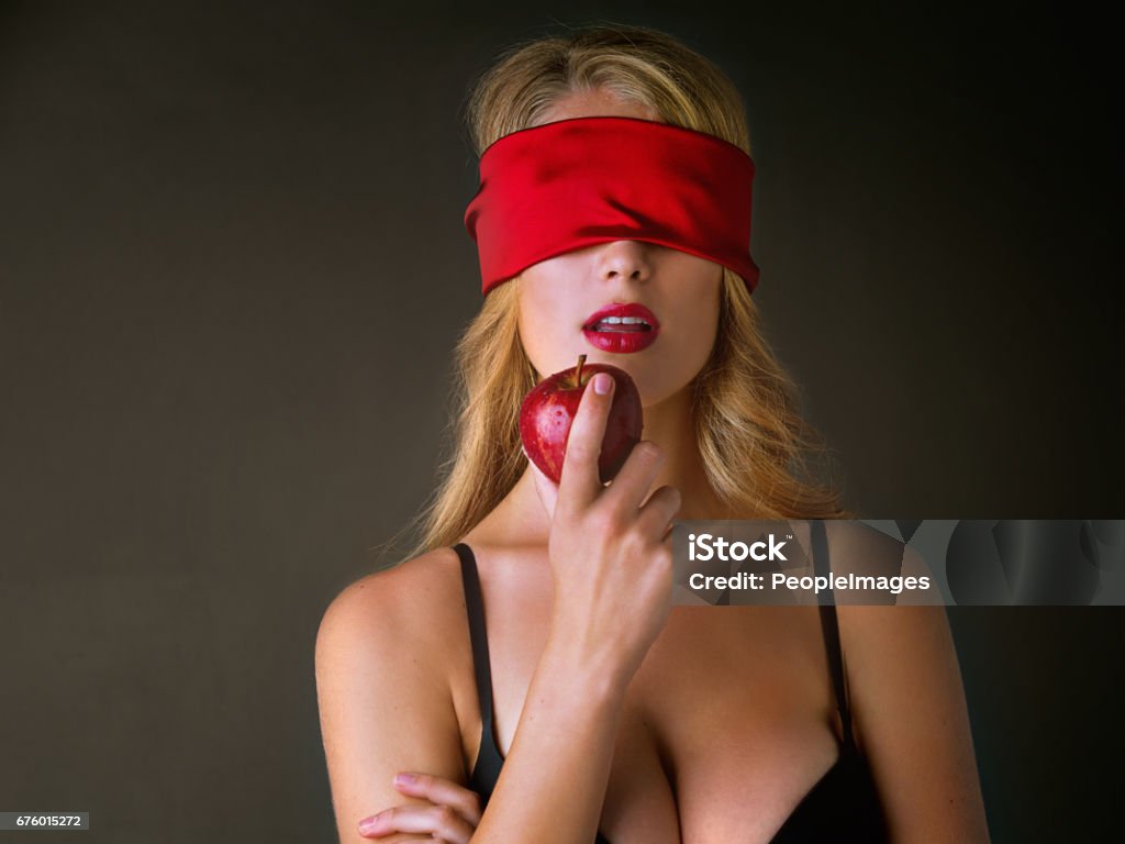 Seducing the senses Studio shot of a blindfolded young woman eating a red apple suggestively against a dark background Blindfold Stock Photo