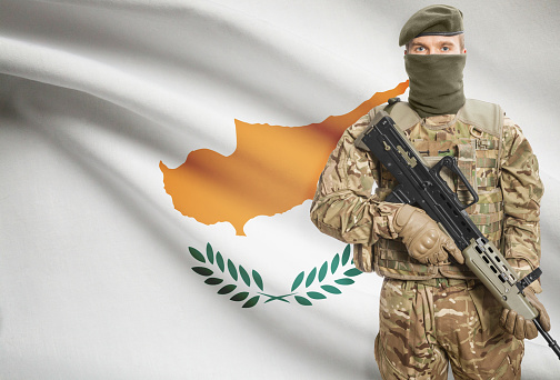 Soldier holding machine gun with national flag on background - Cyprus