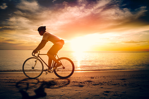 Silhouette of sportsman ride bicycle on lake beach colorful-sunset cloudy sky in background