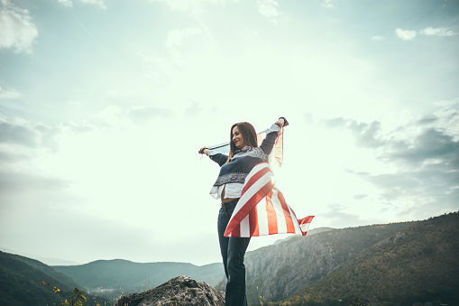 Hipster girl covered in American flag, hiking and having fun in the mountains.