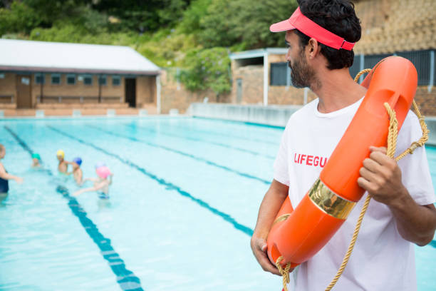 istock Lifeguard with lifebuoy looking at students playing in the pool 676022578