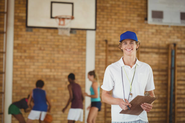 istock Coach smiling at camera while high school team playing basketball in background 676022834