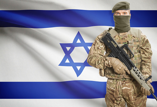 Soldier holding machine gun with national flag on background - Israel