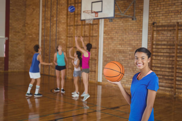 istock High school girl holding a basketball while team playing in background 676023916