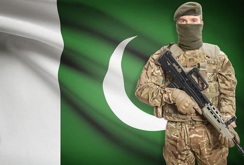 Soldier holding machine gun with national flag on background - Pakistan