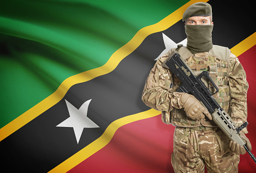Soldier holding machine gun with national flag on background - Saint Kitts and Nevis