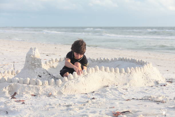 Boy at the beach builds sandcastle.